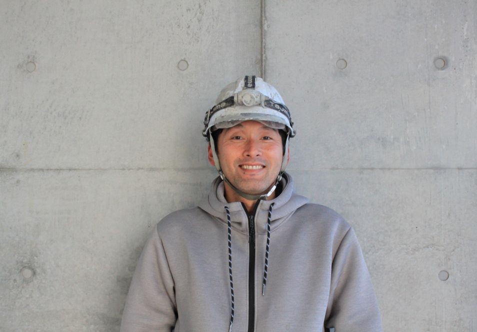 打ち放しコンクリートを背景にしたREPRO株式会社代表取締役のプロフィール写真。建築仕上げと化粧補修を専門とする代表。